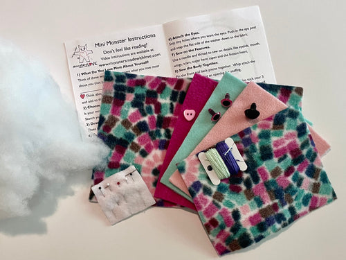 Colorful fabric monsters with attached eyes and ears, and a paper with instructions on a white background.